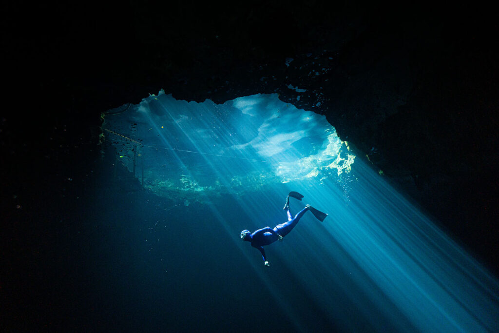 Freedivers ascending in a cenote illuminated by vertical light beams