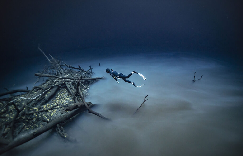 Freediver exploring the surreal underwater landscape of Cenote Angelita in the Yucatán Peninsula, Mexico